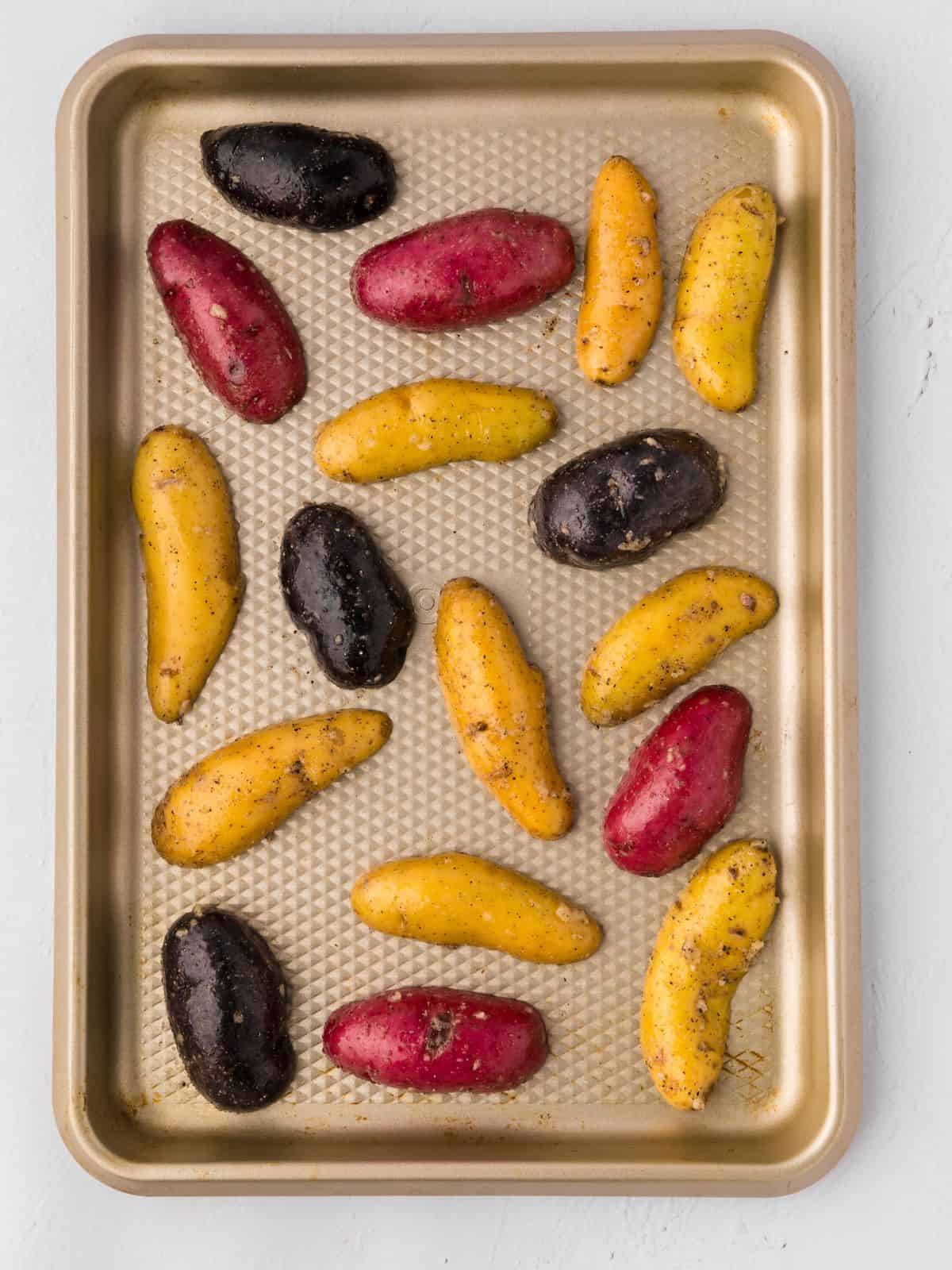Halved fingerling potatoes tossed with garlic and olive oil and butter cut side down on rimmed sheet pan.