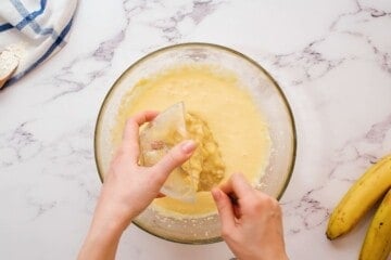 Adding mashed banana to mixing bowl of wet ingredients.