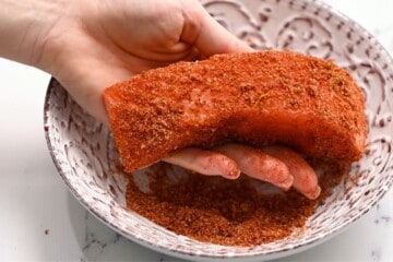 Salmon fillet being coated in the salmon seasoning in a small bowl.