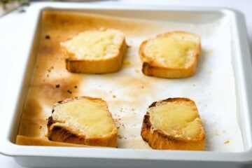 Toasted French Bread on sheet pan topped with Swiss cheese and Parmesan Cheese after baking until browned.