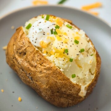 Air Fried Baked Potato on gray plate cut open and topped with dollop of butter, sour cream, chives, cheddar, and pepper.