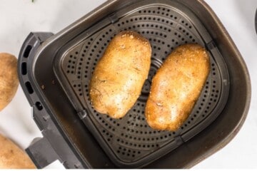 Seasoned russet potatoes inside basket of air fryer.