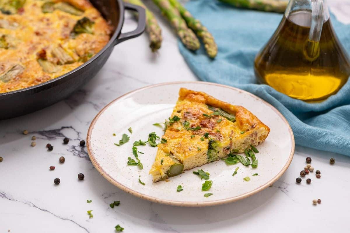 Slice of Asparagus Frittata on white plate next to baked frittata.