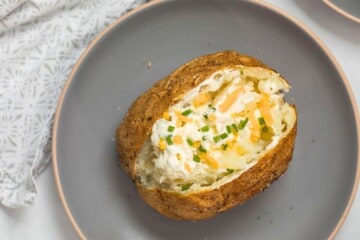 Air Fried Baked Potato on gray plate cut open and topped with dollop of butter, sour cream, cheddar, and pepper and chives.