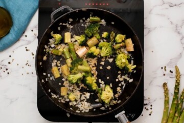 Broccoli, asparagus, and onions being sauteed in cast iron skillet.