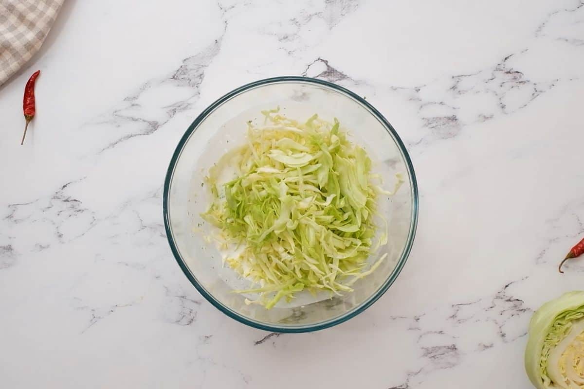 Green cabbage in mixing bowl with creamy cilantro lime sauce.