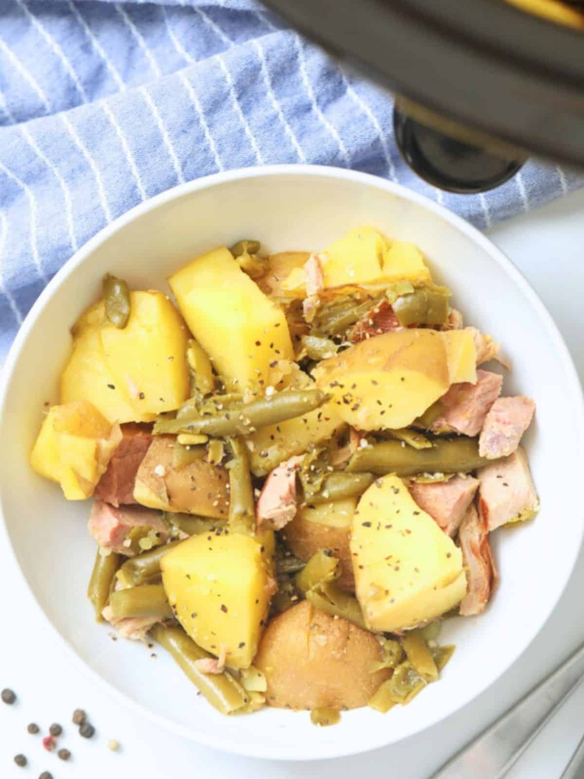 Bowl of potatoes with diced ham and green beans next to crockpot.