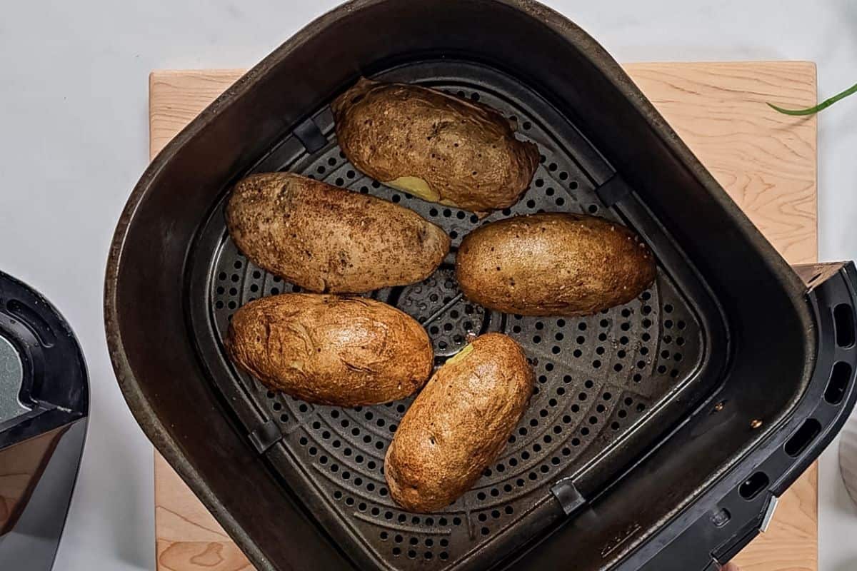 Potato Skins skin side up in air fryer after being brushed with butter and salt and pepper.