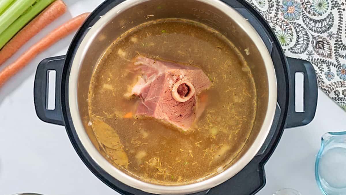 Ingredients for split pea soup inside inner pot with ham bone.