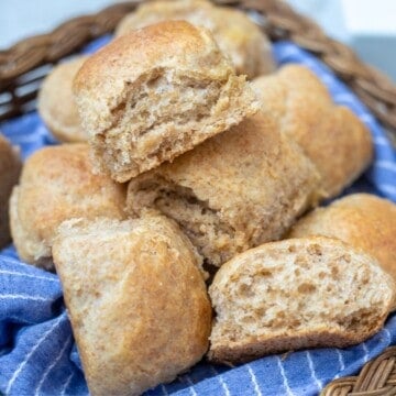 Freshly baked whole wheat rolls in basket lined with blue napkin.