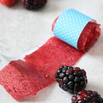 A homemade fruit roll-up rolled up in blue craft paper with blackberries and strawberries to the side.
