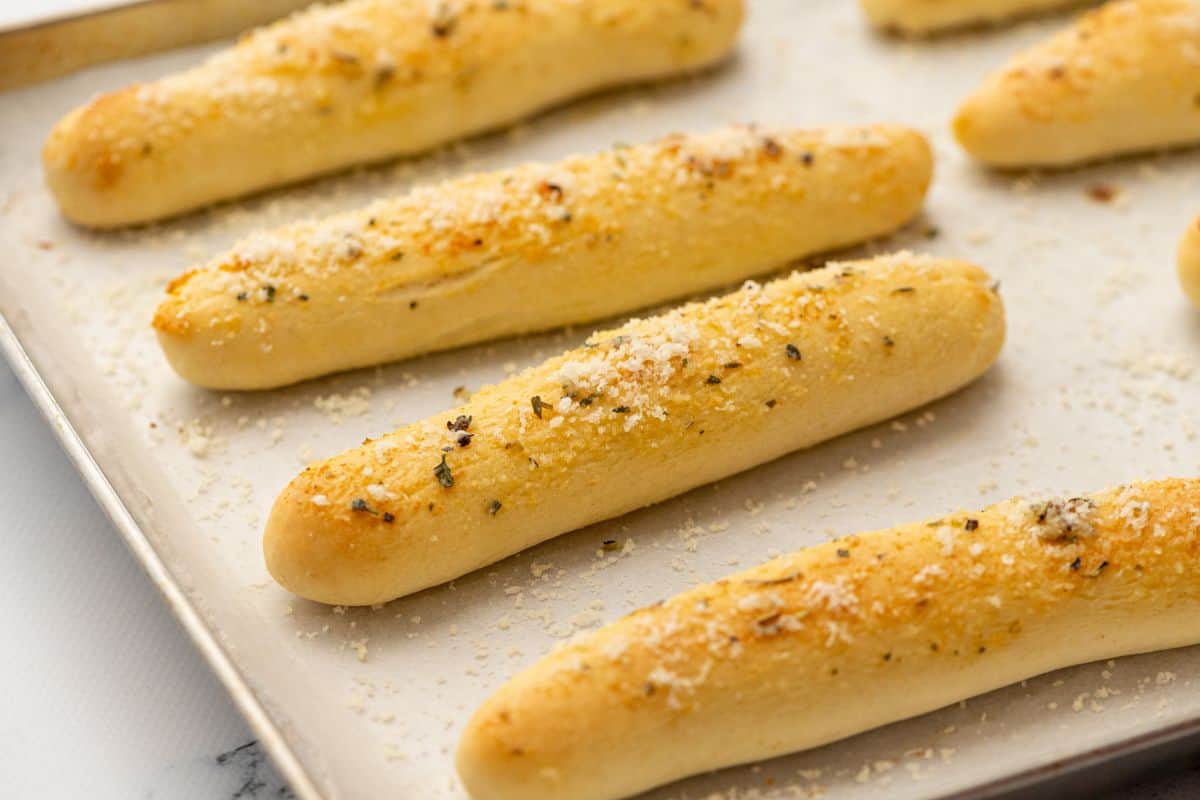 Baked breadsticks on a baking sheet brushed with garlic butter and parmesan.