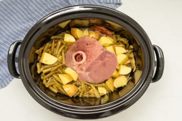 Slow cooker with ham bone, potatoes, and green beans inside.