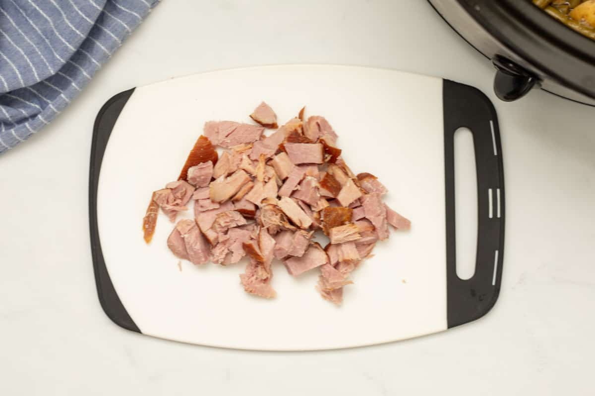 Diced ham on white cutting board with crockpot off in distance.
