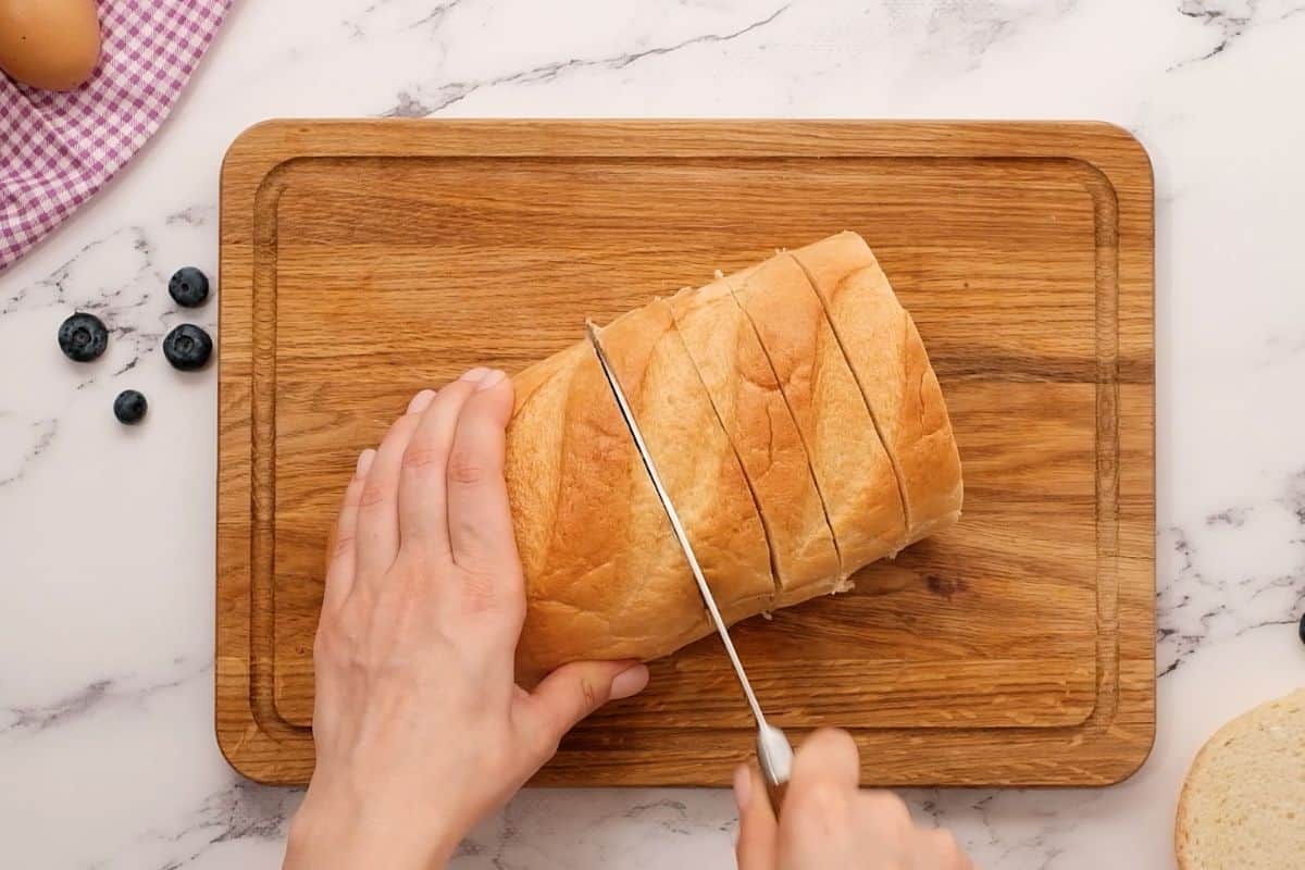 Knife cutting French Loaf into 1-inch thick slices.