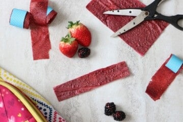 Fruit leather cut into strips next to fresh fruit and lunchbox.