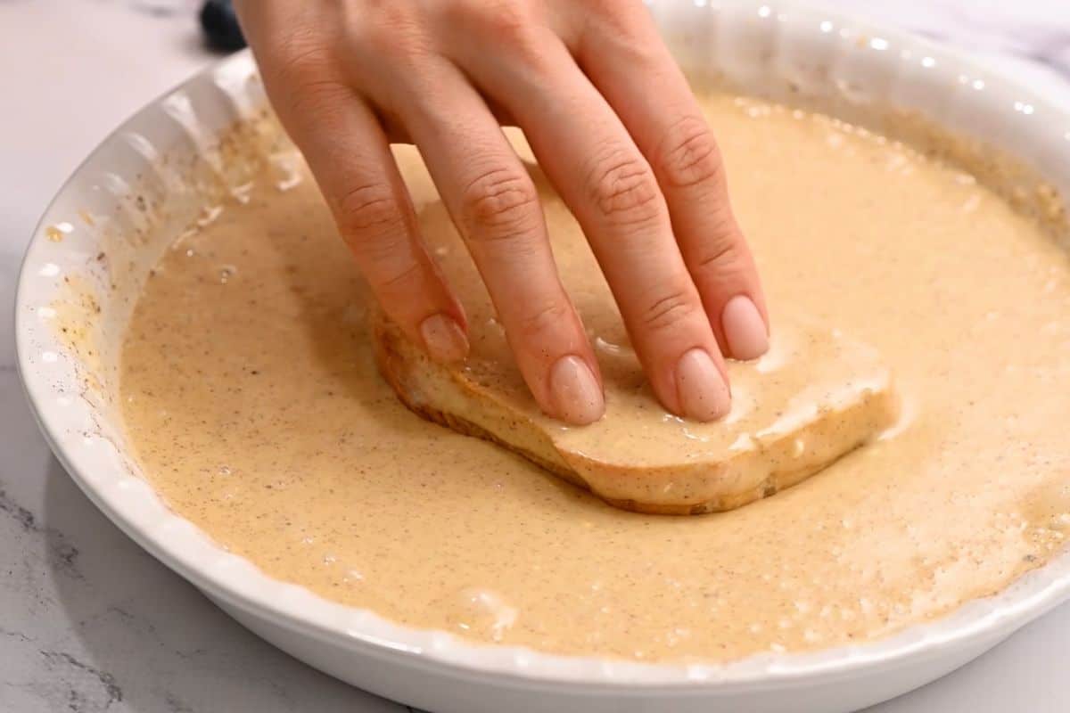 Slice of French bread being dipped into egg custard to make French toast.