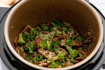 Beef and broccoli with brown sauce topped with sesame seeds and green onions inside inner pot of pressure cooker.