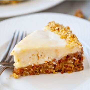 Slice of Instant Pot Carrot Cake Cheesecake slice on white plate showing layered carrot cake with creamy cheesecake.