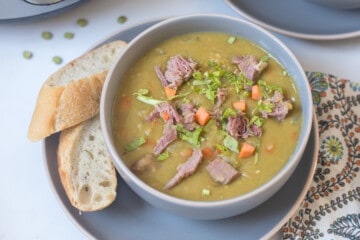 Bowl of Instant Pot split pea soup topped with diced ham and carrots served next to crusty bread.