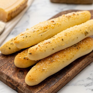 Soft homemade breadsticks on wooden cutting board after being brushed with garlic butter.