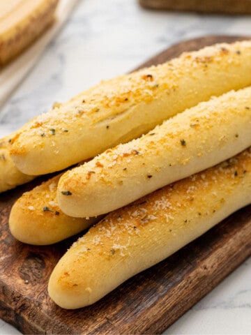 Soft homemade breadsticks on wooden cutting board after being brushed with garlic butter.