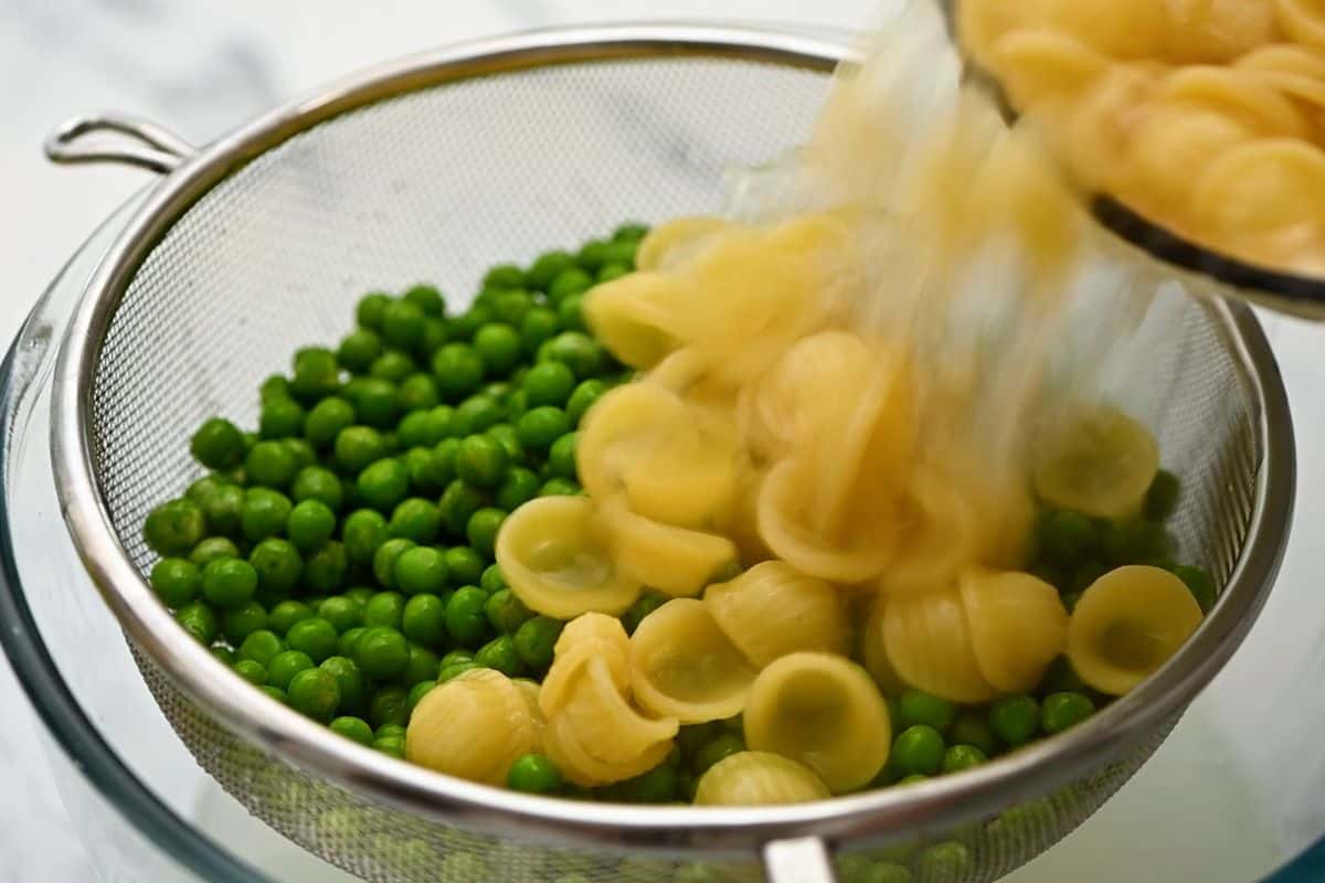 Cooked pasta being poured over peas in fine mesh colander.