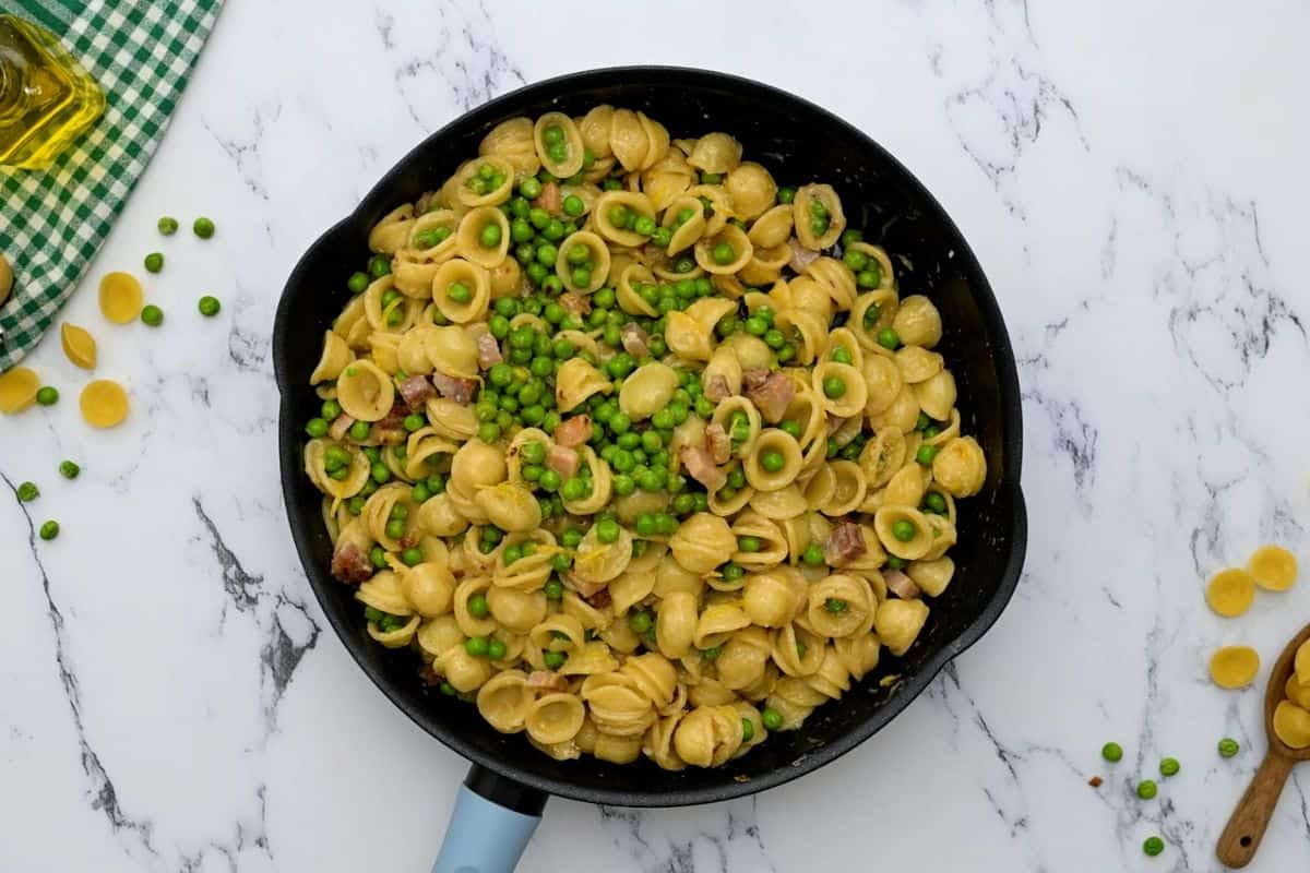 Bowl of pasta with peas, pancetta, and parmesan in skillet after being tossed together.