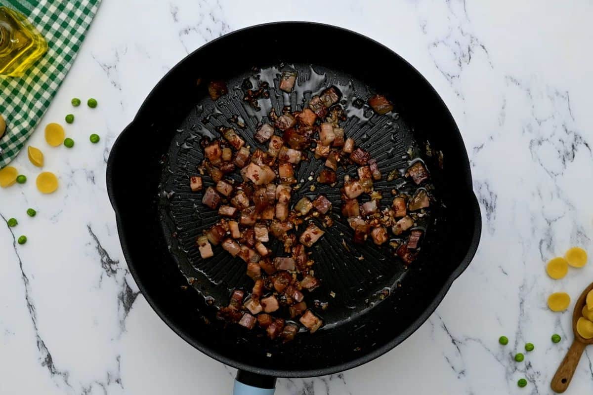 Pancetta and shallots in saute pan after being sauteed together and fat rendered out.