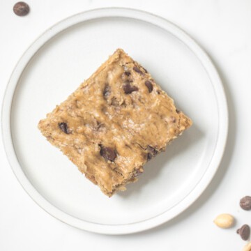 A slice of a banana bar with chocolate chips on a white plate with peanut and chocolate chips on the side.