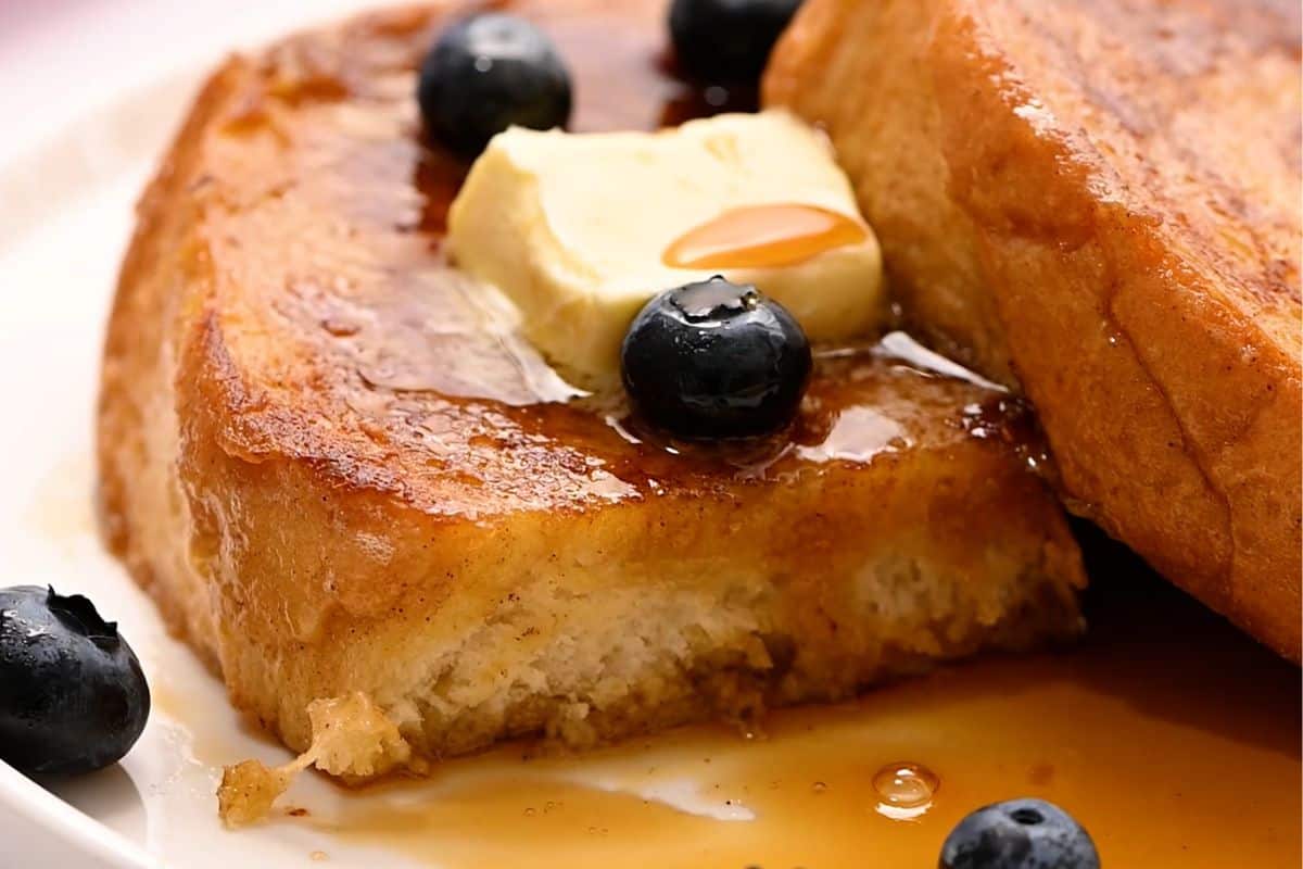 French Toast sliced open to reveal crispy exterior and fluffy interior served with maple and blueberries.