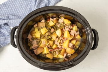 Slow cooker with ham, green beans, and potatoes inside crockpot.