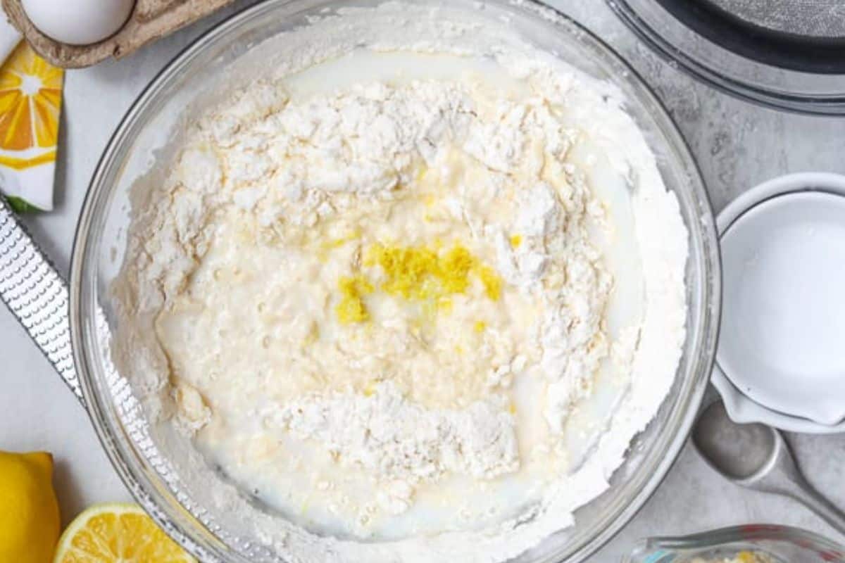 Flour, buttermilk, lemon zest, and creamed mixture for lemon bread in mixing bowl.