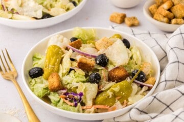 Copycat Olive Garden salad made with iceberg lettuce mix, olives, tomatoes, and croutons in large white serving bowl next fork.