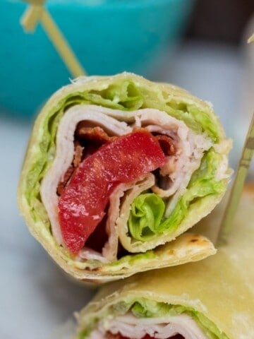 Turkey Wrap with tomatoes, bacon, lettuce and avocado cut open and held together with toothpicks.