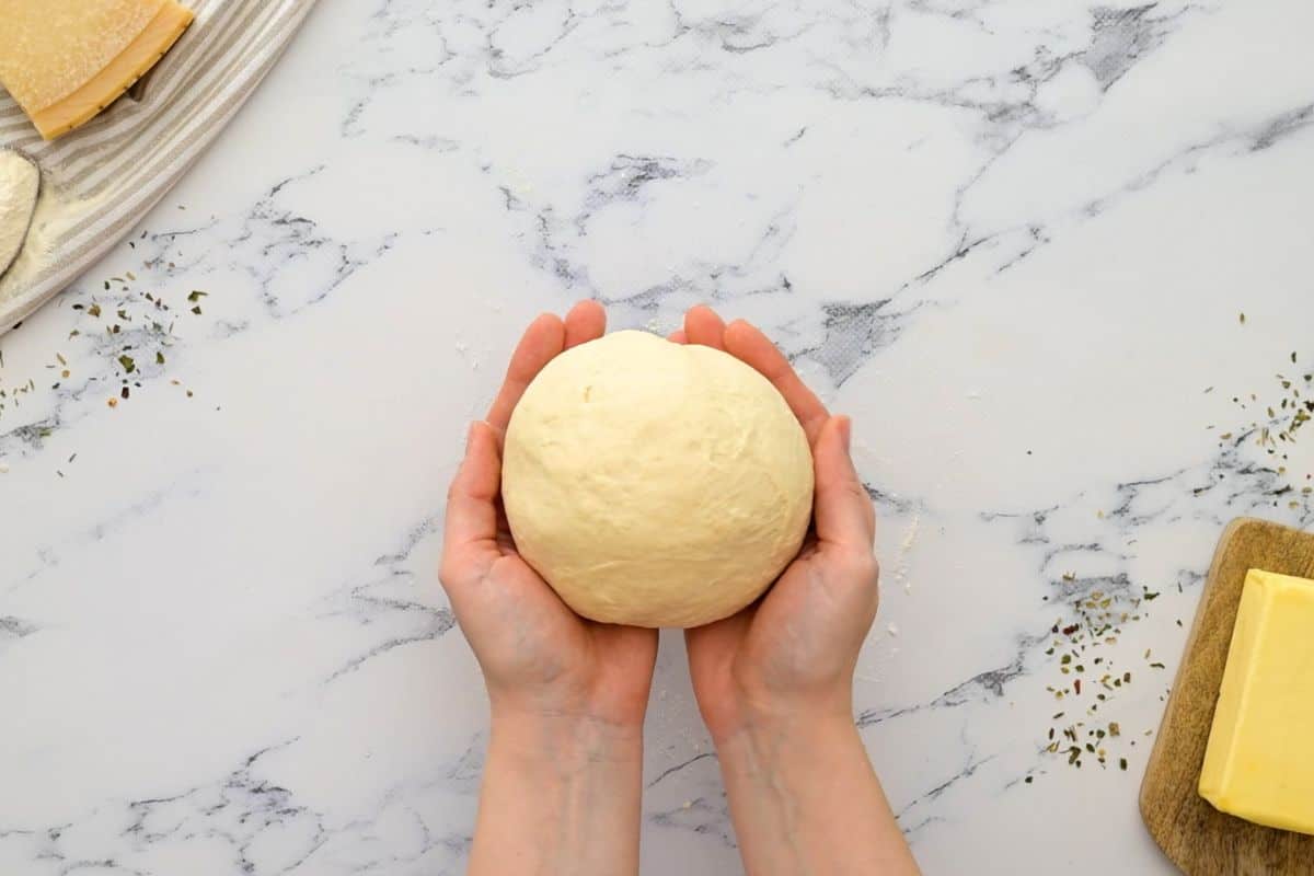 Dough ball held in two hands after being kneaded until smooth and elastic.