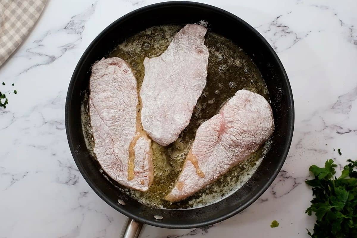 Chicken cutlets coated with flour in saute pan with butter and olive oil.