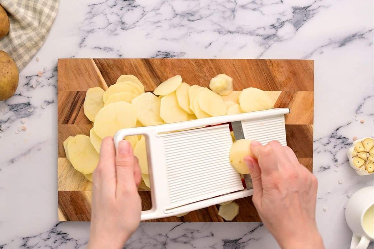 Showing slicing potatoes on a mandoline into thin slices.