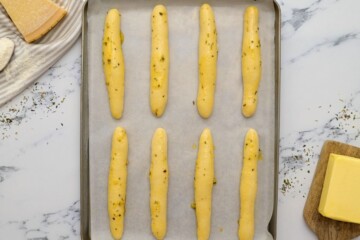 8 shaped breadsticks on parchment lined baking sheet brushed with garlic butter and Italian seasoning.