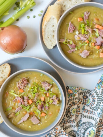 Two bowls of Instant Pot split pea soup topped with diced ham and carrots served next to crusty bread.
