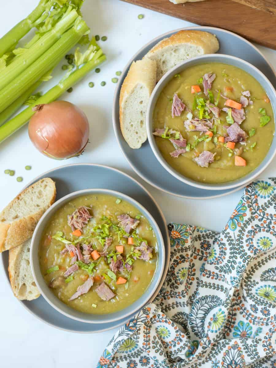 Two bowls of Instant Pot split pea soup topped with diced ham and carrots served next to crusty bread.
