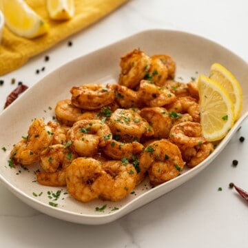 Platter of seasoned air fryer shrimp topped with parsley and served with lemon wedges.