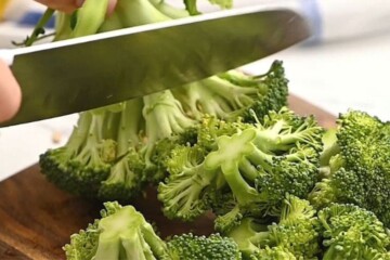 Knife cutting broccoli florets off broccoli stem.