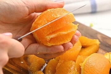Knife cutting segments of oranges from whole orange.