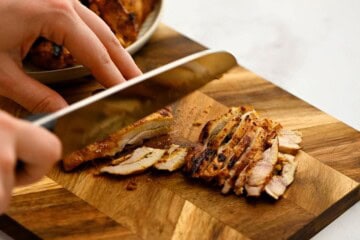 Grilled chicken shawarma on cutting board being cut into bite-sized pieces.