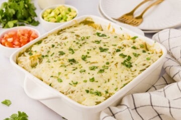 Baked green salsa chicken enchiladas in white baking dish topped with minced cilantro.