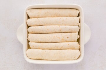Flour tortillas filled with shredded chicken and salsa verde in a white baking dish.