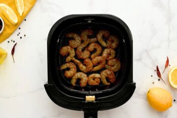 Seasoned shrimp in single layer in air fryer basket.