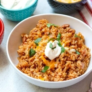Instant Pot Rice and Beans made with dried beans in white bowl topped with cheese, sour cream, and cilantro.