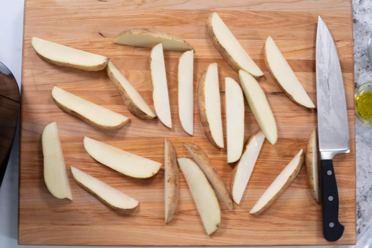 Sliced potato wedges on cutting board next to butcher's knife.